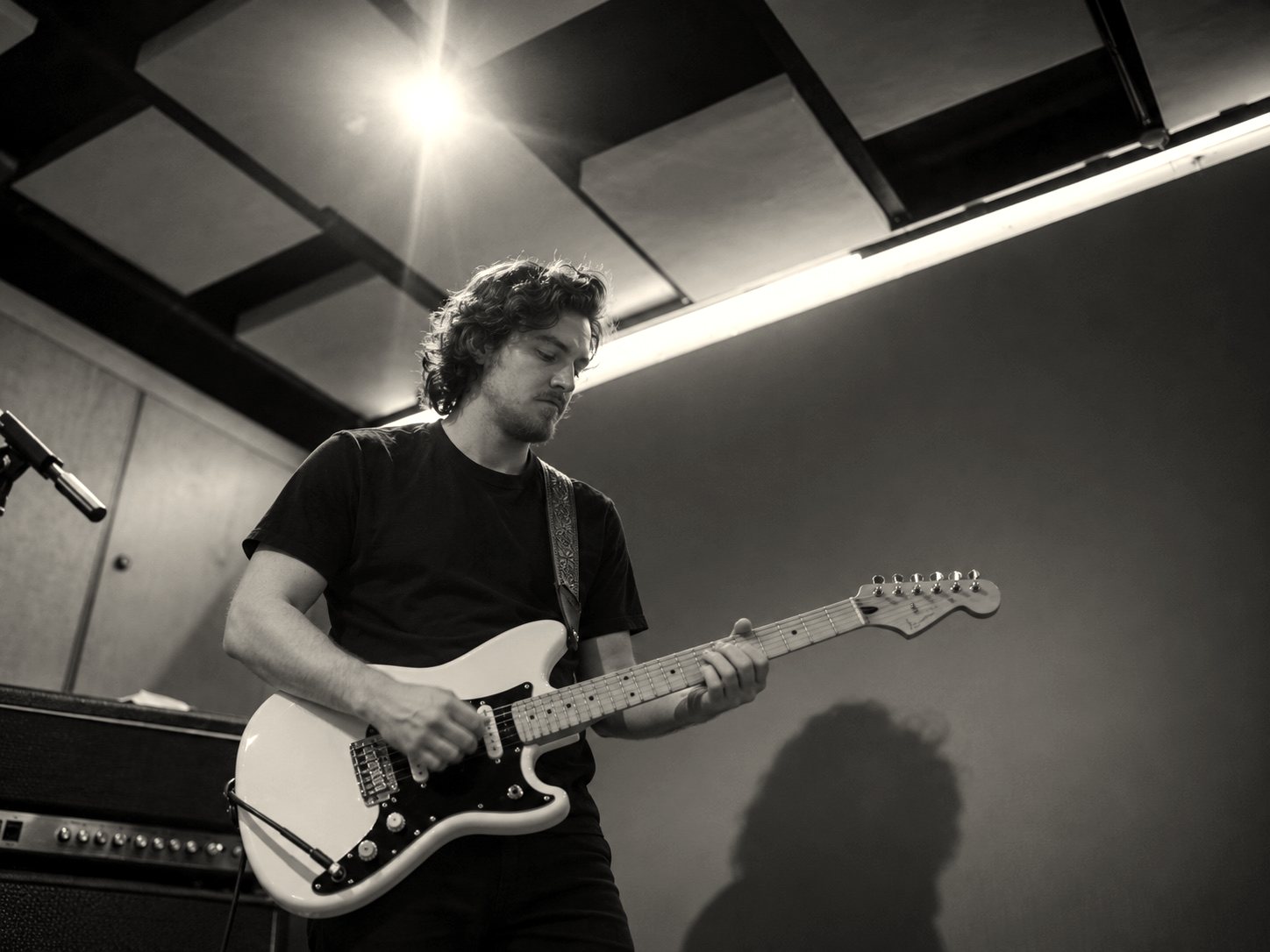Adam Cole playing a white electric guitar in a rehearsal room